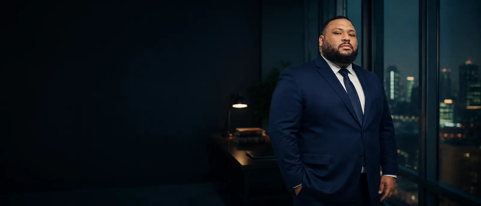 Dr. Bruno Moraes, advogado, em pé num escritório à noite com a cidade ao fundo pela janela